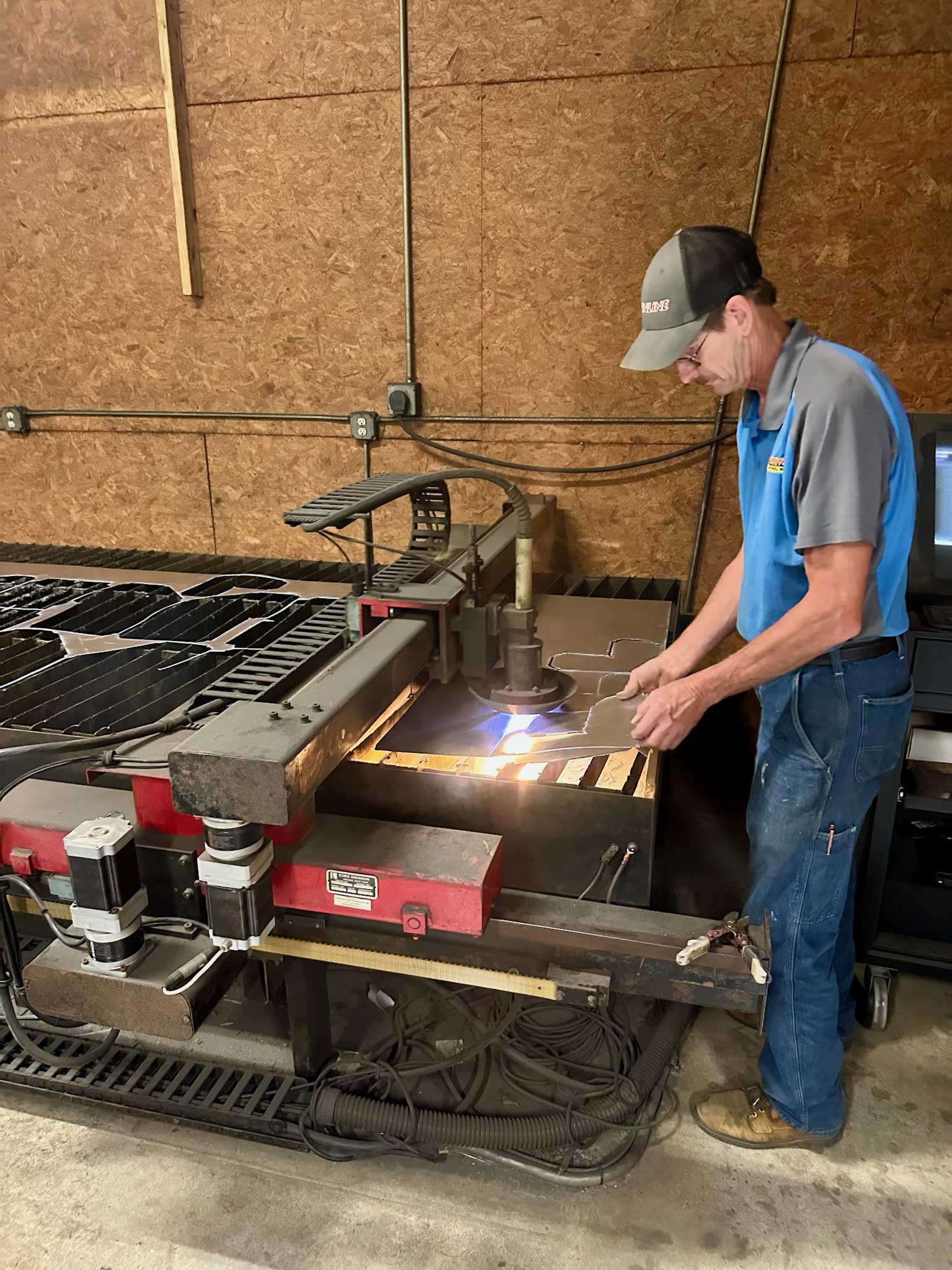 A man operating a CNC plasma cutter cutting metal sheets on a workshop table.